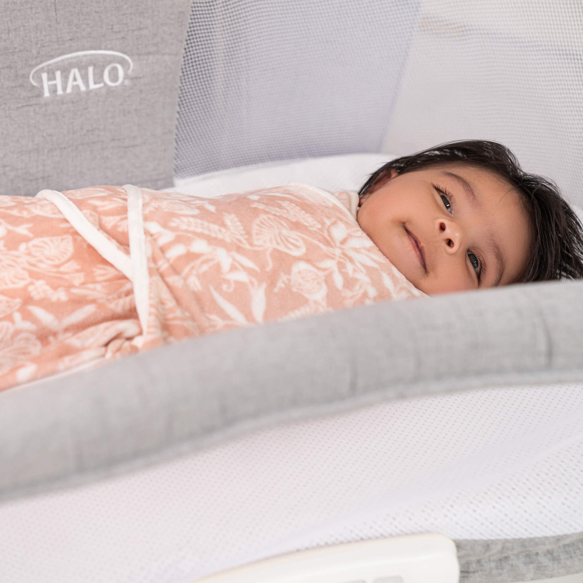 Baby swaddled in soft pink Garden print velboa wrap lying comfortably in a HALO bassinet.