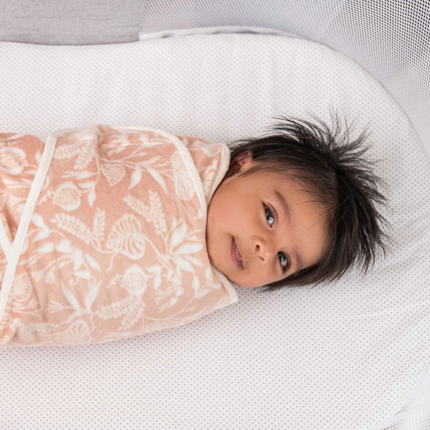 Baby smiling in a plush aden + anais velboa wrap with a floral print from the Garden swaddle set.