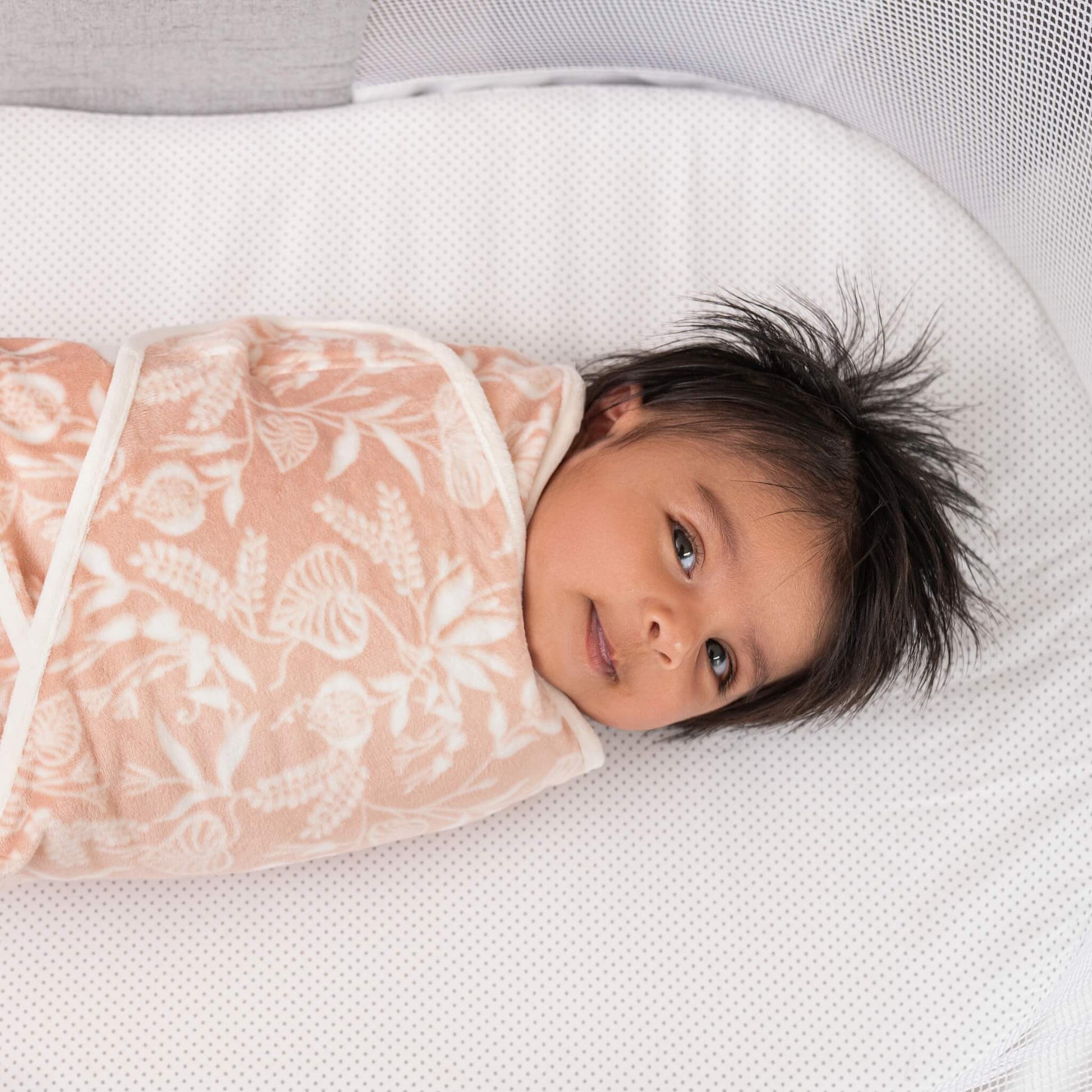 Baby smiling in a plush aden + anais velboa wrap with a floral print from the Garden swaddle set.
