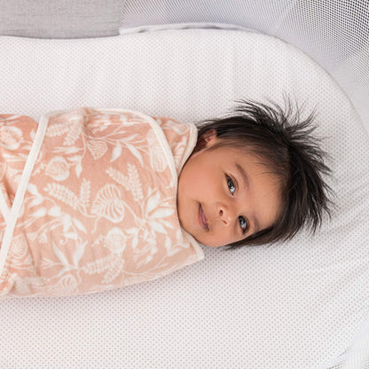 Baby smiling in a plush aden + anais velboa wrap with a floral print from the Garden swaddle set.