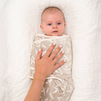 Close-up of mother’s hand gently resting on a baby swaddled in the beige Rockland Marsh velboa wrap, lying on a soft white blanket.