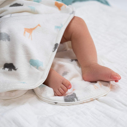 Baby’s legs and feet peek out from under the safari print swaddle, lying on a soft quilt.