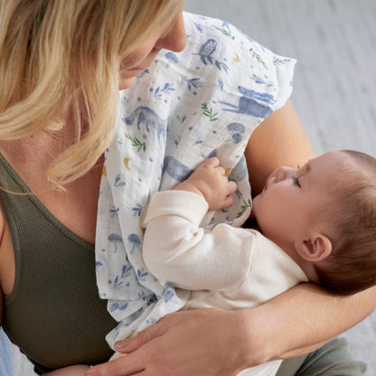 Mother cuddling baby using aden + anais organic muslin swaddle blanket with deer and woodland print.
