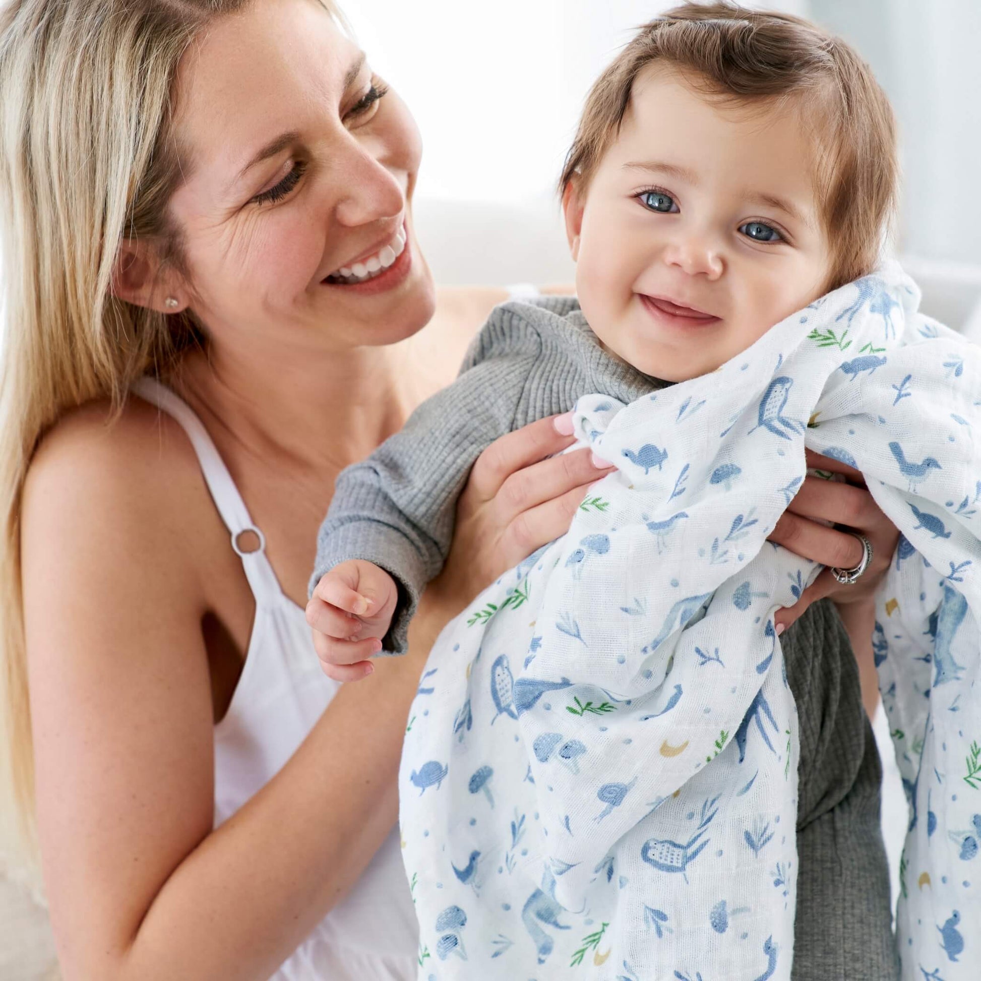 Baby held in aden + anais Outdoors swaddle with soft forest animals and plants design in breathable cotton.