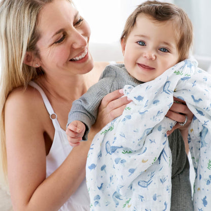 Baby held in aden + anais Outdoors swaddle with soft forest animals and plants design in breathable cotton.