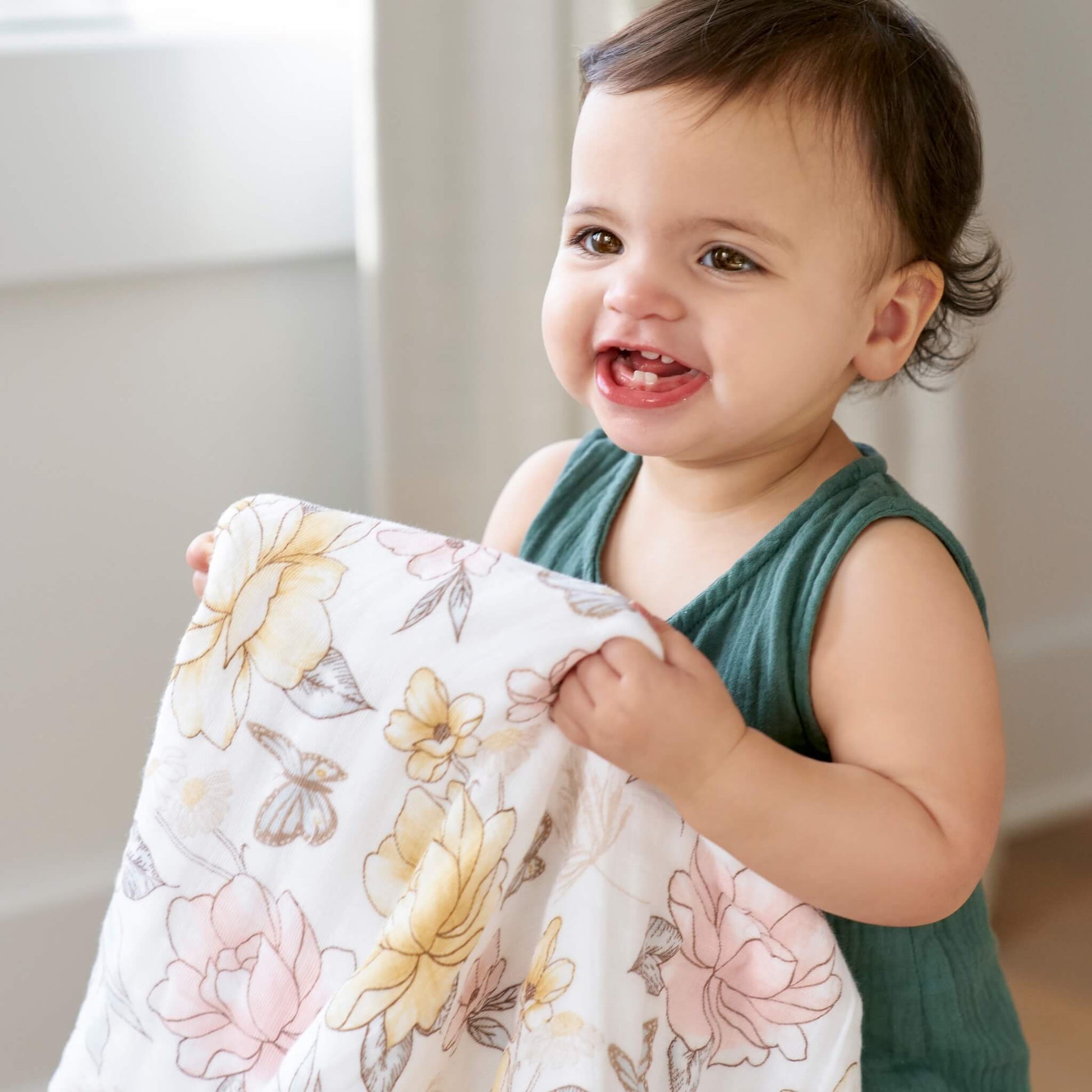 Baby holding the aden + anais dream blanket in Earthly floral print. GOTS certified cotton muslin, soft and breathable for everyday comfort.