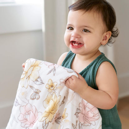 Baby holding the aden + anais dream blanket in Earthly floral print. GOTS certified cotton muslin, soft and breathable for everyday comfort.