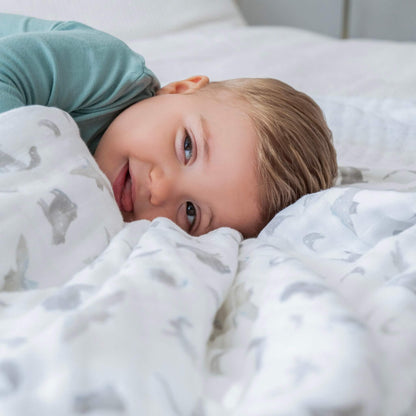 Little one resting on the aden + anais organic cotton muslin blanket, with grey celestial animal print. Gentle, breathable, and soft on delicate skin.
