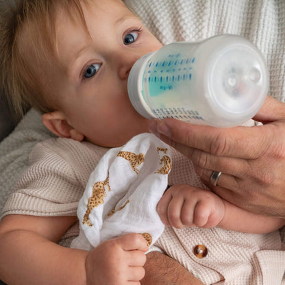 Close-up of a baby being bottle-fed while holding an Aden + Anais organic muslin square in Safari Dreams print.