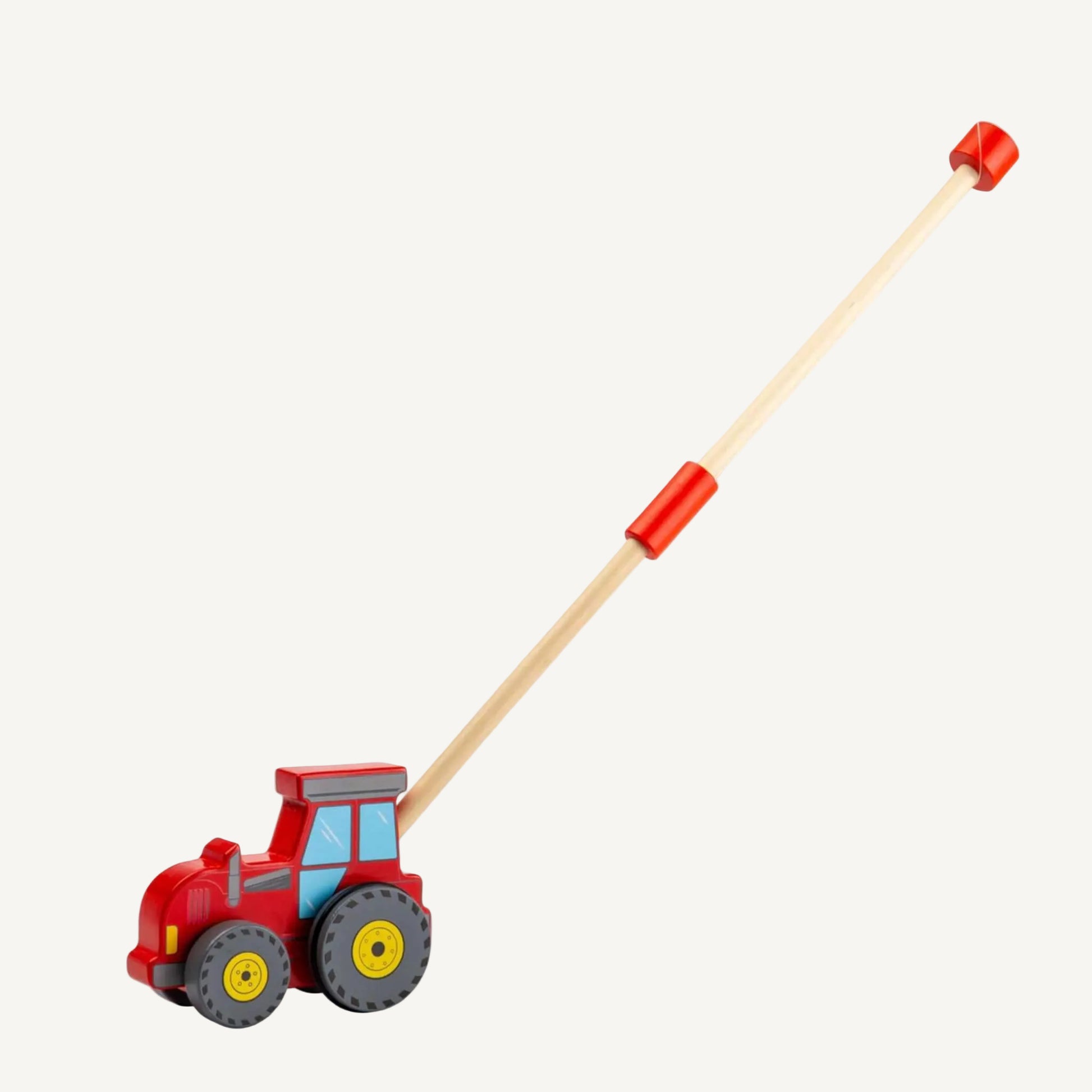 Red wooden tractor push along toy with a long natural wood handle extended behind it, featuring chunky grey wheels, yellow wheel centres and painted cab windows.