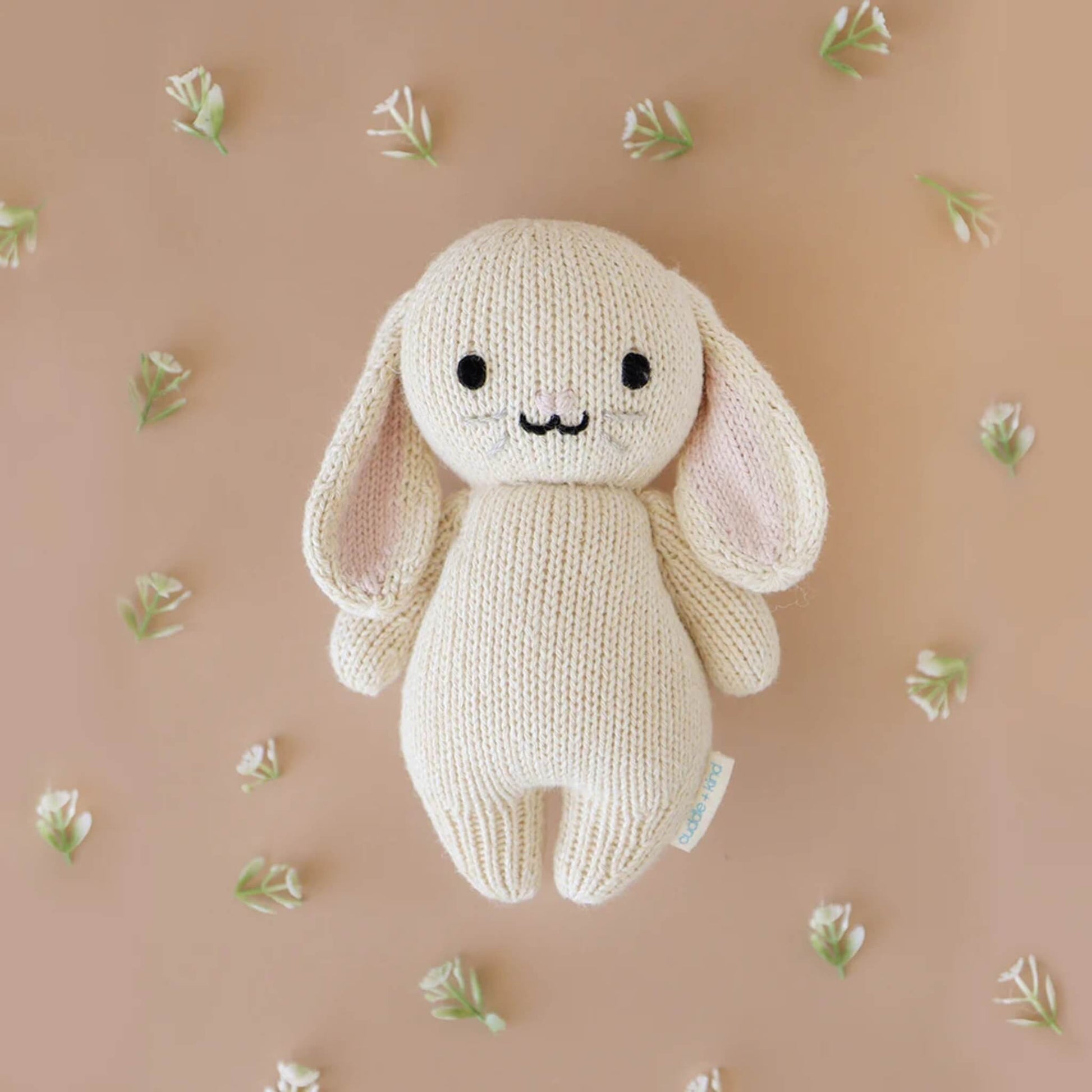 A knitted bunny soft toy placed on a neutral background surrounded by small delicate flowers.