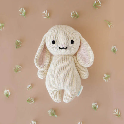 A knitted bunny soft toy placed on a neutral background surrounded by small delicate flowers.