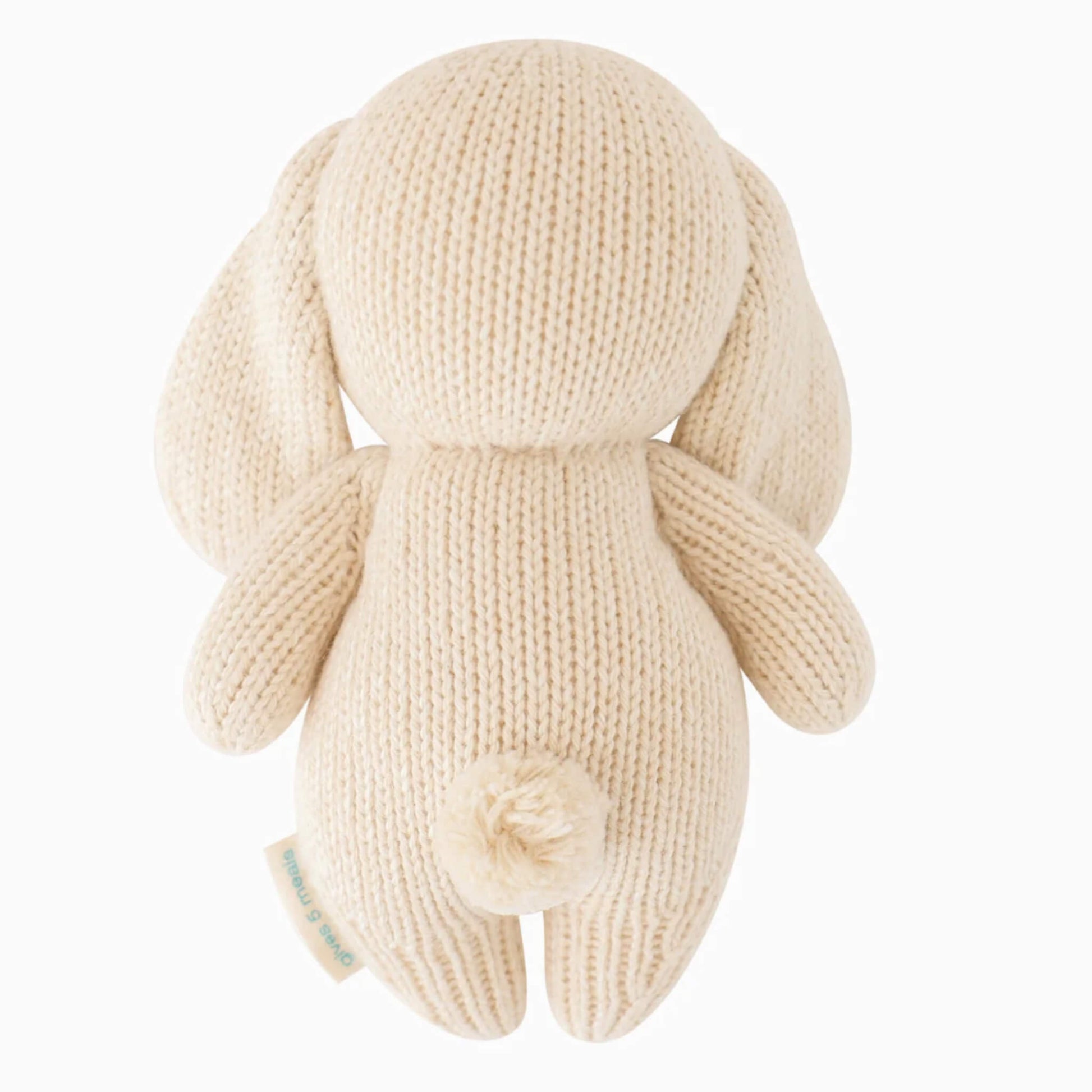 Back view of knitted bunny soft toy showing rounded shape, floppy ears and pom-pom tail.