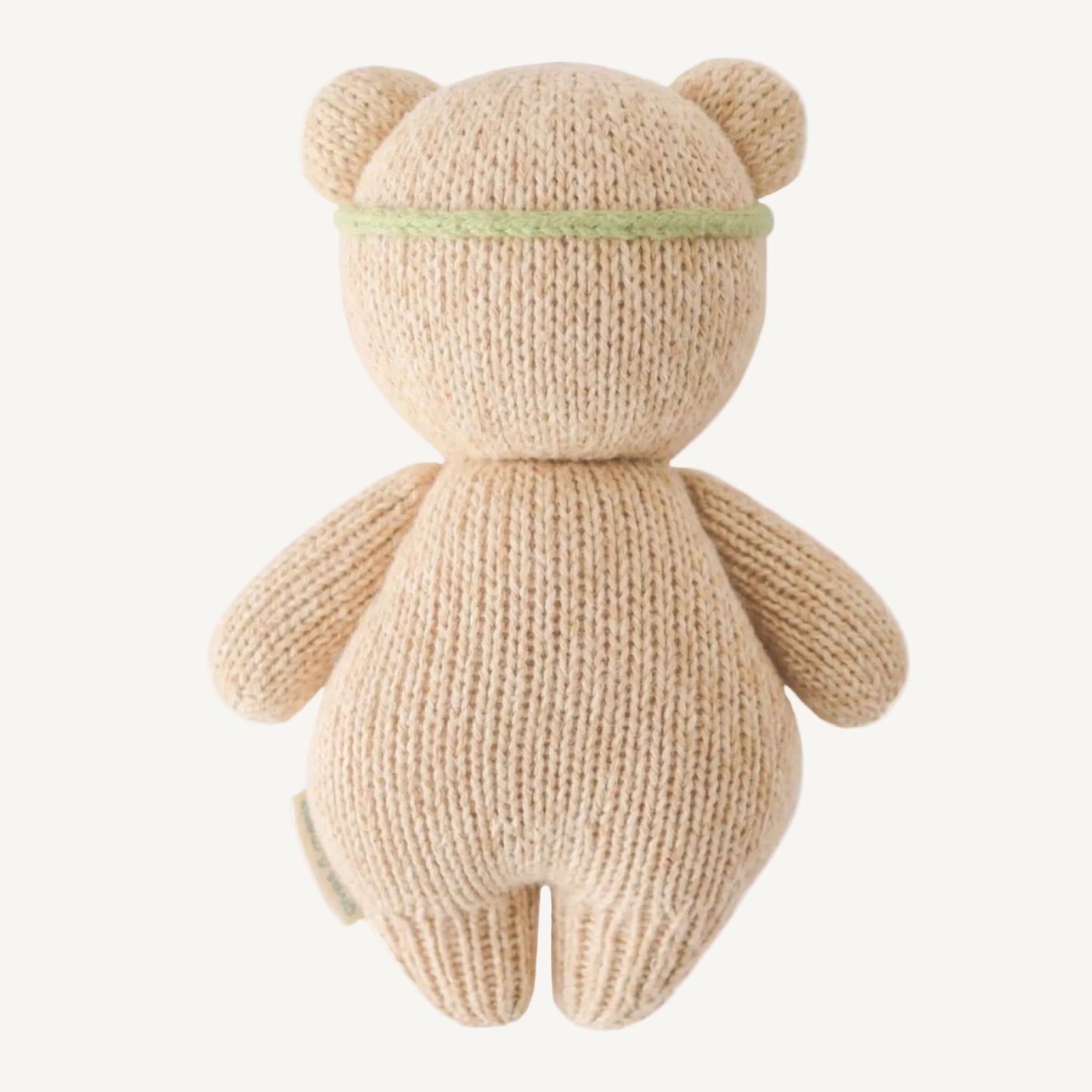 Rear view of a soft knitted teddy bear showing smooth stitching and a simple green band around the head.