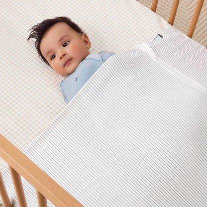 Baby lying under the HugMe Blanket in midnight stripe, showing the secure fit across the cot mattress.