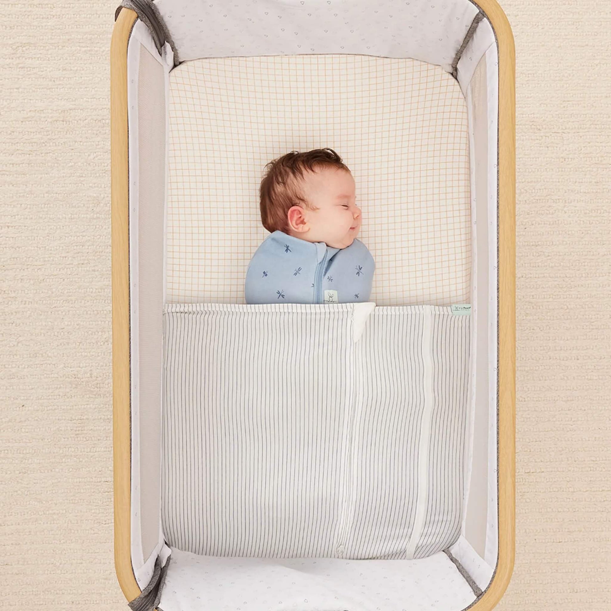 Sleeping baby swaddled under the HugMe Blanket in midnight stripe, fitted neatly around the mattress.