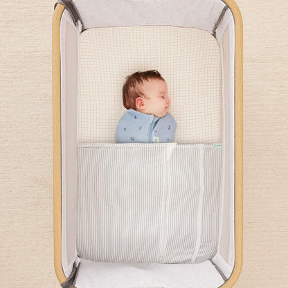 Sleeping baby swaddled under the HugMe Blanket in midnight stripe, fitted neatly around the mattress.