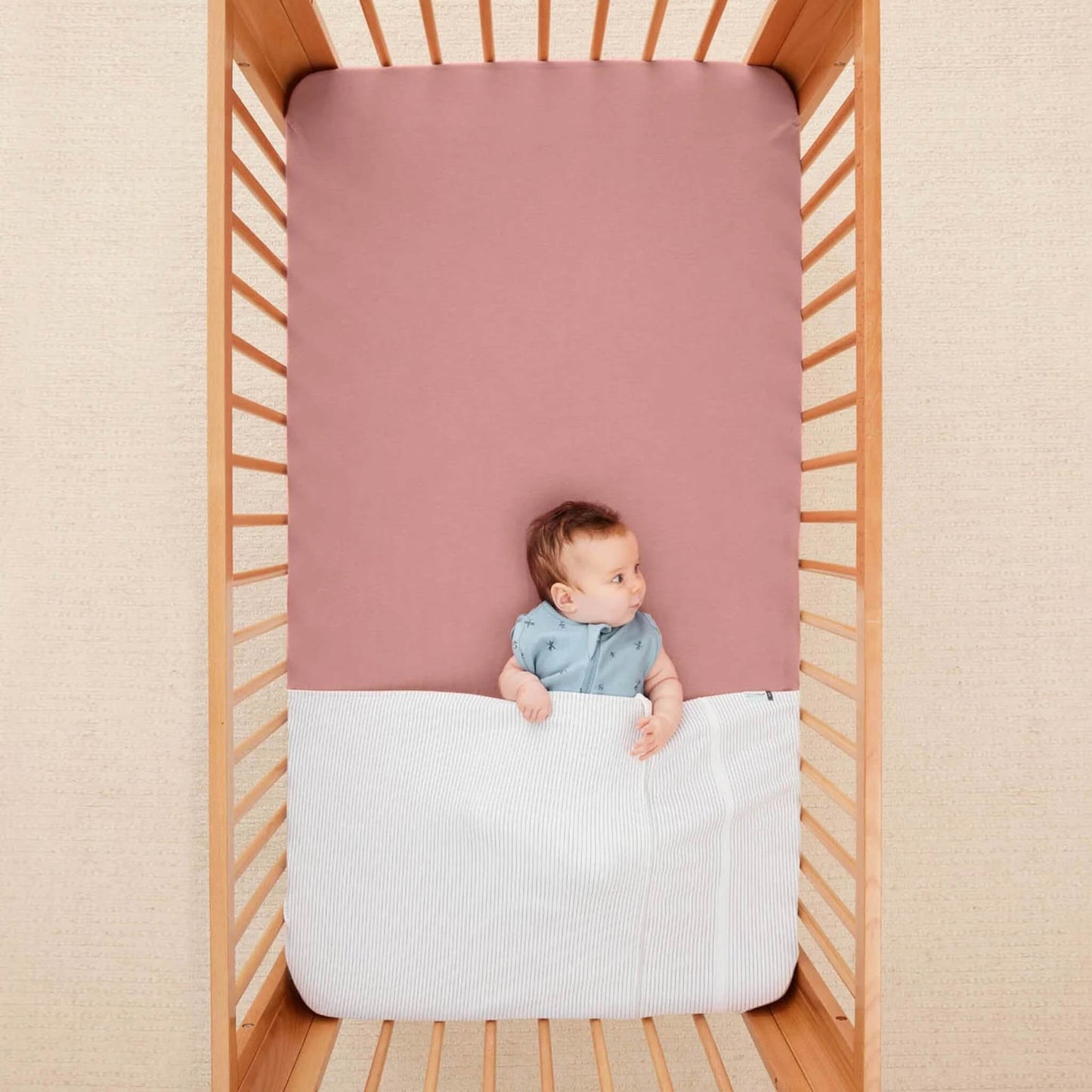 Baby resting under the HugMe Blanket in midnight stripe with a soft rose sheet for contrast.