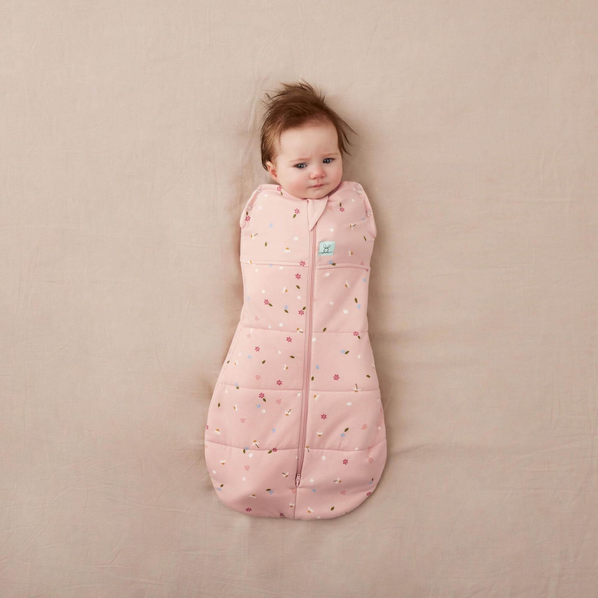 Baby wrapped snugly in a Winter Swaddle Bag (2.5 Tog) with pink floral print, zip-up front, and bell-shaped bottom.