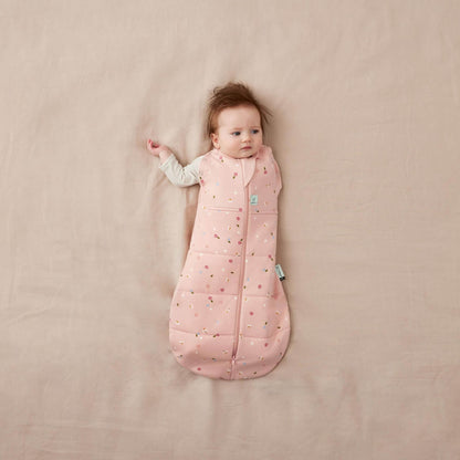 Baby lying comfortably in a Swaddle Bag with a daisies design,. Shown with one arm out, and zipped-up front.