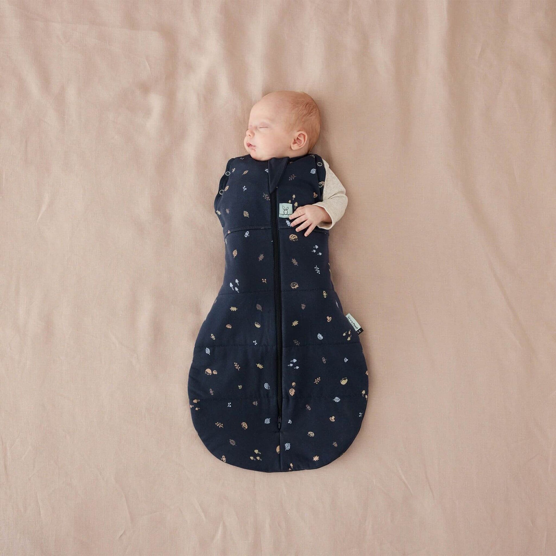 Baby lying comfortably in a 2.5 TOG winter weight swaddle Bag with a hedgehog design. Shown with one arm in and one arm out.