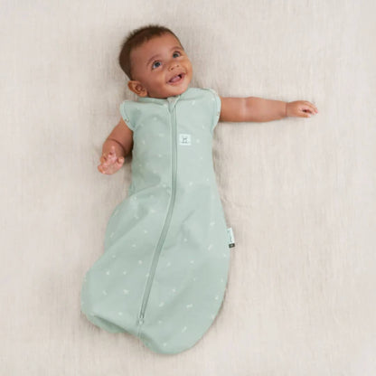 Baby resting with both arms out in a sage green Cocoon Swaddle Bag, worn as a sleeveless baby sleeping bag.