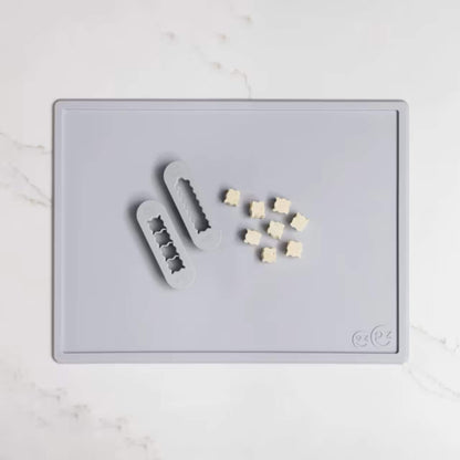 Grey silicone food cutters beside small cubes of soft food prepared for baby finger foods on a matching placemat.