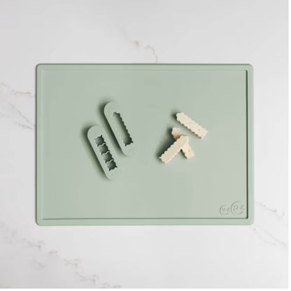Sage green silicone food cutters beside small cubes of soft food prepared for baby finger foods on a matching cutting board.
