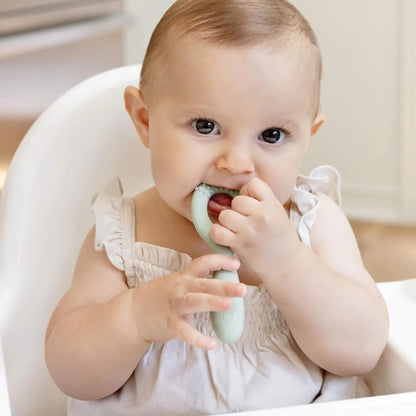 Baby biting a loop-handle silicone oral development tool with textured bumps that massage gums and encourage oral motor movement.
