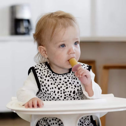 Baby sitting in a highchair holding and eating a frozen popsicle made for baby-led weaning and teething relief.