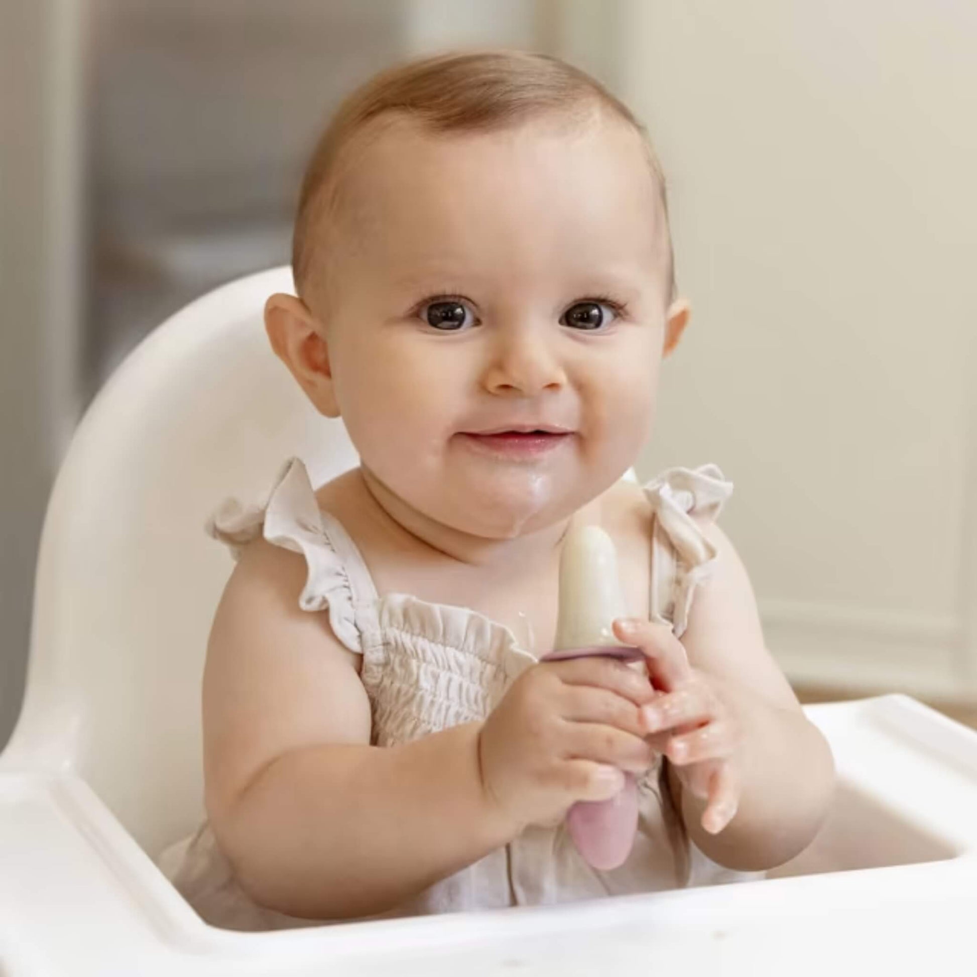 Baby sitting in a highchair holding a frozen baby popsicle made with milk or purée designed for baby-led weaning and teething relief.