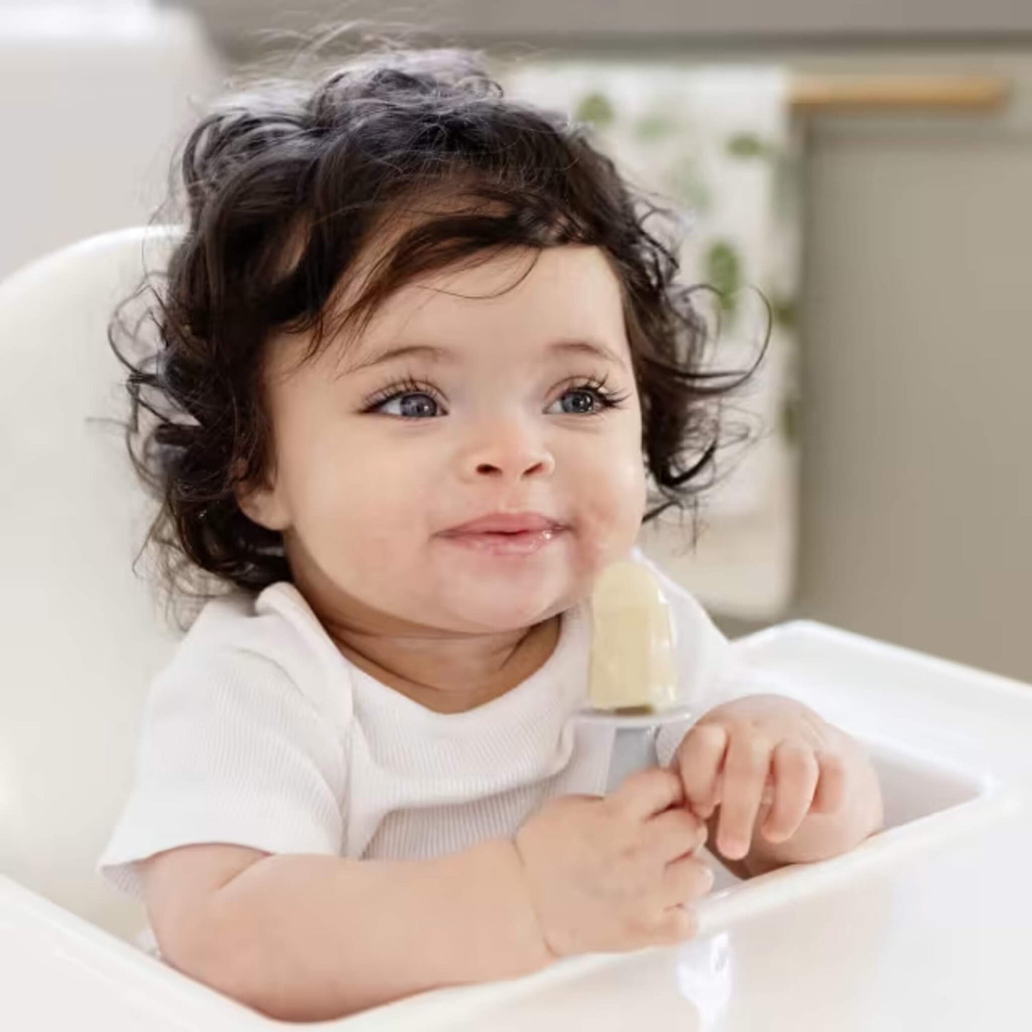 Baby sitting in a highchair holding a frozen baby popsicle designed for baby-led weaning and teething relief.