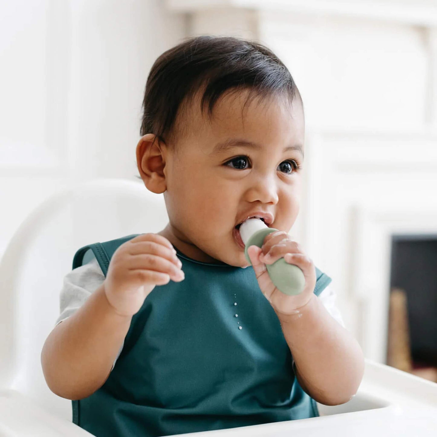 Baby wearing a bib chewing on a frozen baby popsicle designed for teething relief and early self-feeding practice.