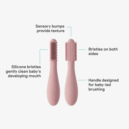 Two blush silicone baby toothbrushes displayed with labelled features showing sensory bumps for texture, silicone bristles for gentle cleaning and a handle designed for baby-led brushing.