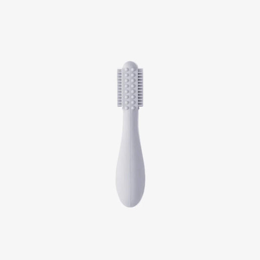 Grey silicone baby toothbrush showing soft bristles on both sides with raised sensory bumps along a rounded head and a thick easy-grip handle for small hands.
