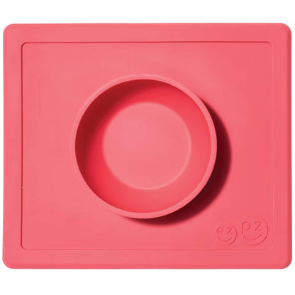 ezpz Happy Bowl in coral. A round silicone bowl is built into a rectangular placemat with the ezpz smiley face logo embossed in the corner.