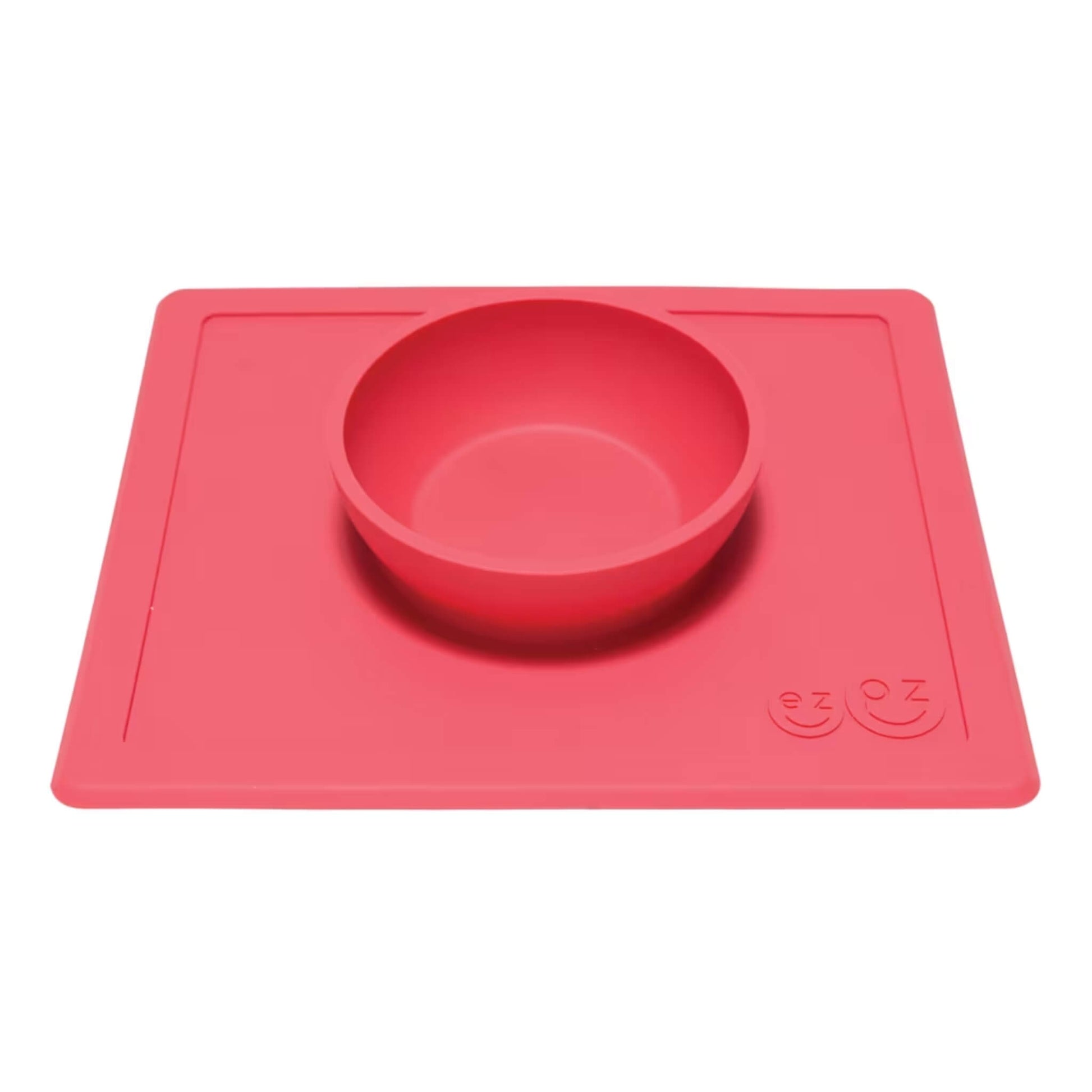 Coral silicone bowl attached to a flat rectangular placemat, shown from an angle to highlight the depth of the bowl.