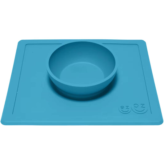 Blue silicone feeding bowl attached to a flat rectangular placemat, shown from an angle to highlight the depth of the bowl.