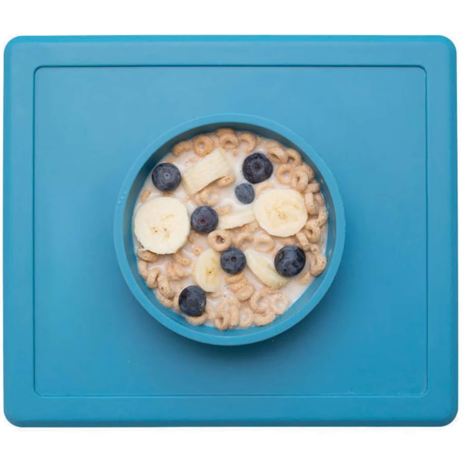 Child's silicone placemat in blue with a built-in bowl neatly filled with cereal, milk, banana slices and blueberries.