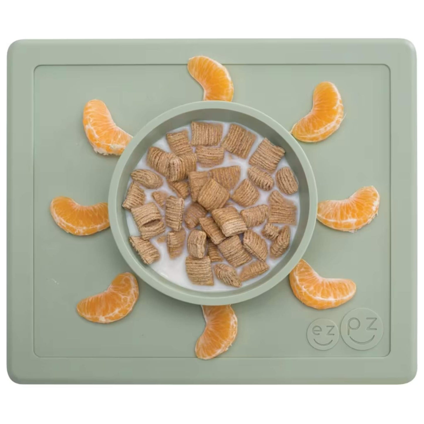 Sage green silicone placemat with built-in bowl containing cereal squares and milk, surrounded by orange segments neatly placed around the edge of the mat.