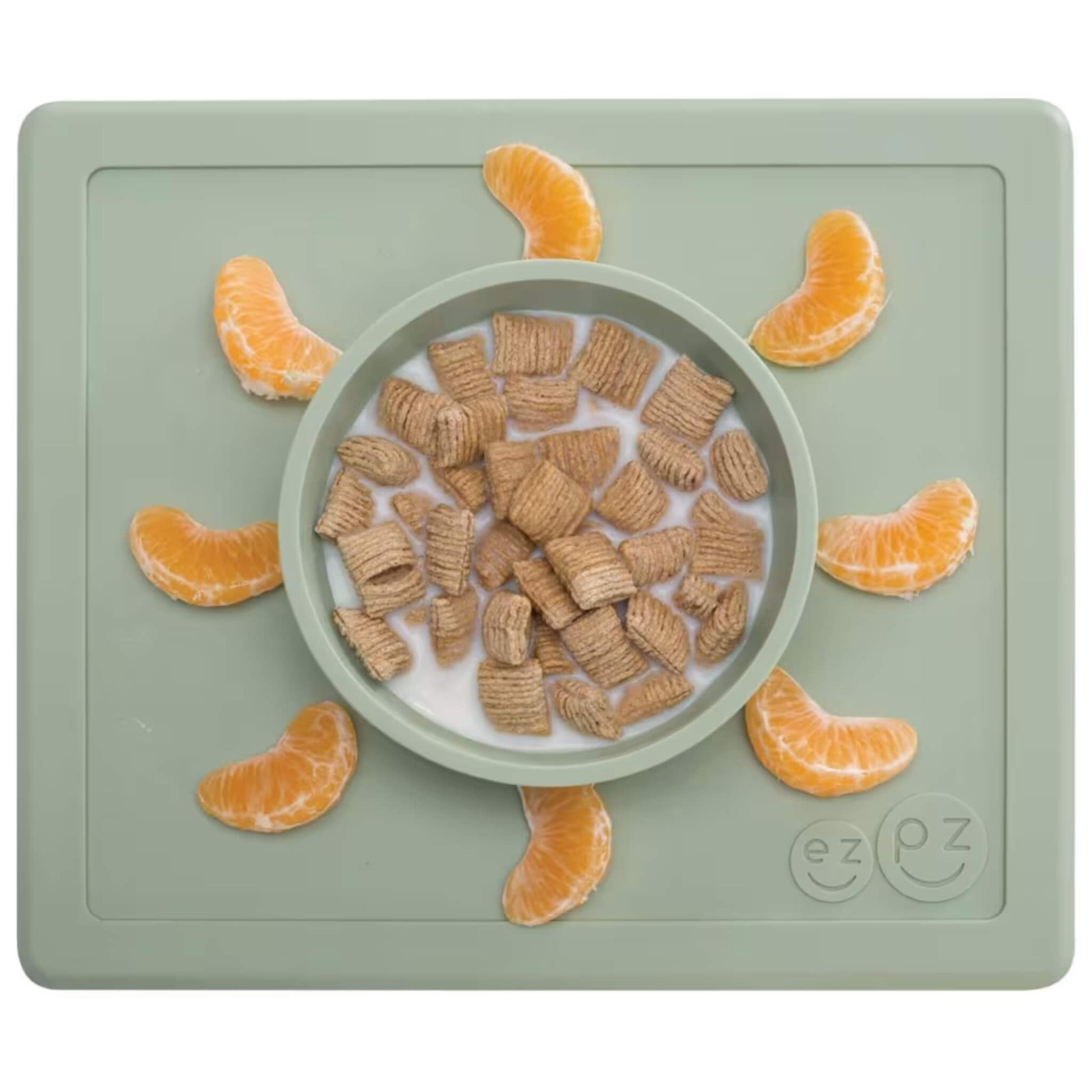 Sage green silicone placemat with built-in bowl containing cereal squares and milk, surrounded by orange segments neatly placed around the edge of the mat.