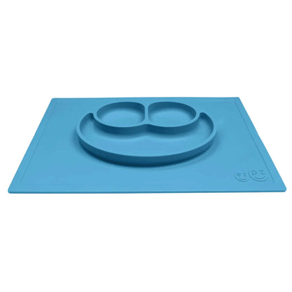 A blue silicone placemat with an integrated plate shown from an angle, featuring three compartments shaped like a smiley face.