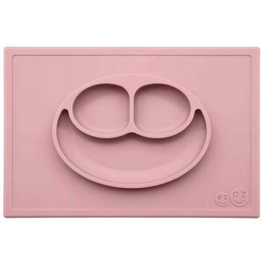 Ezpz Happy Mat in blush pink, a silicone placemat and plate in one with three compartments in a smiley face design to make toddler mealtimes easier.