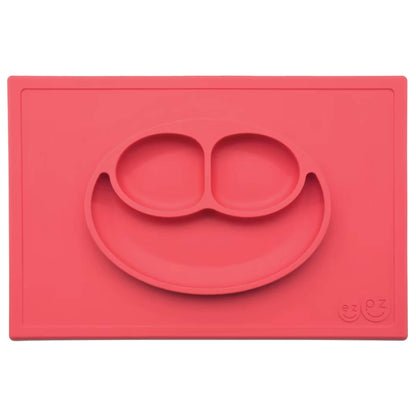 Ezpz Happy Mat in coral red, a silicone placemat and plate in one with three compartments in a smiley face design to make toddler mealtimes easier.