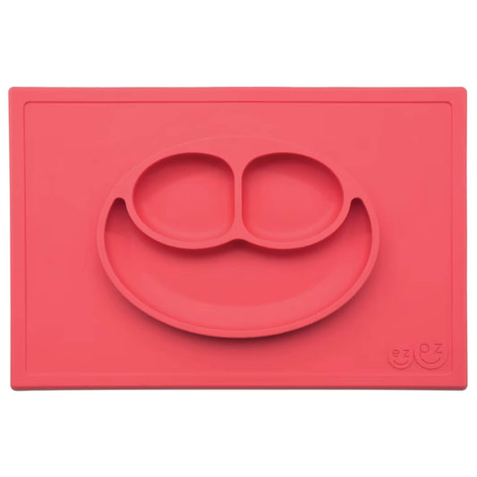 Ezpz Happy Mat in coral red, a silicone placemat and plate in one with three compartments in a smiley face design to make toddler mealtimes easier.