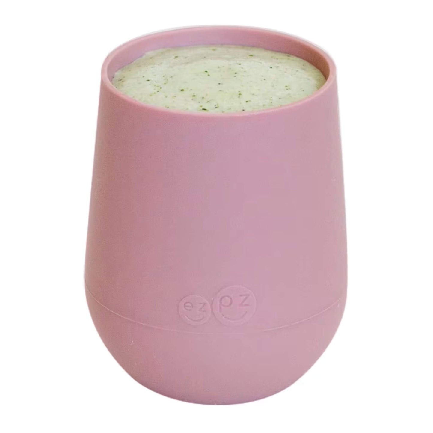 A blush pink silicone training cup shown filled with milk, designed for toddlers learning to drink from an open cup.