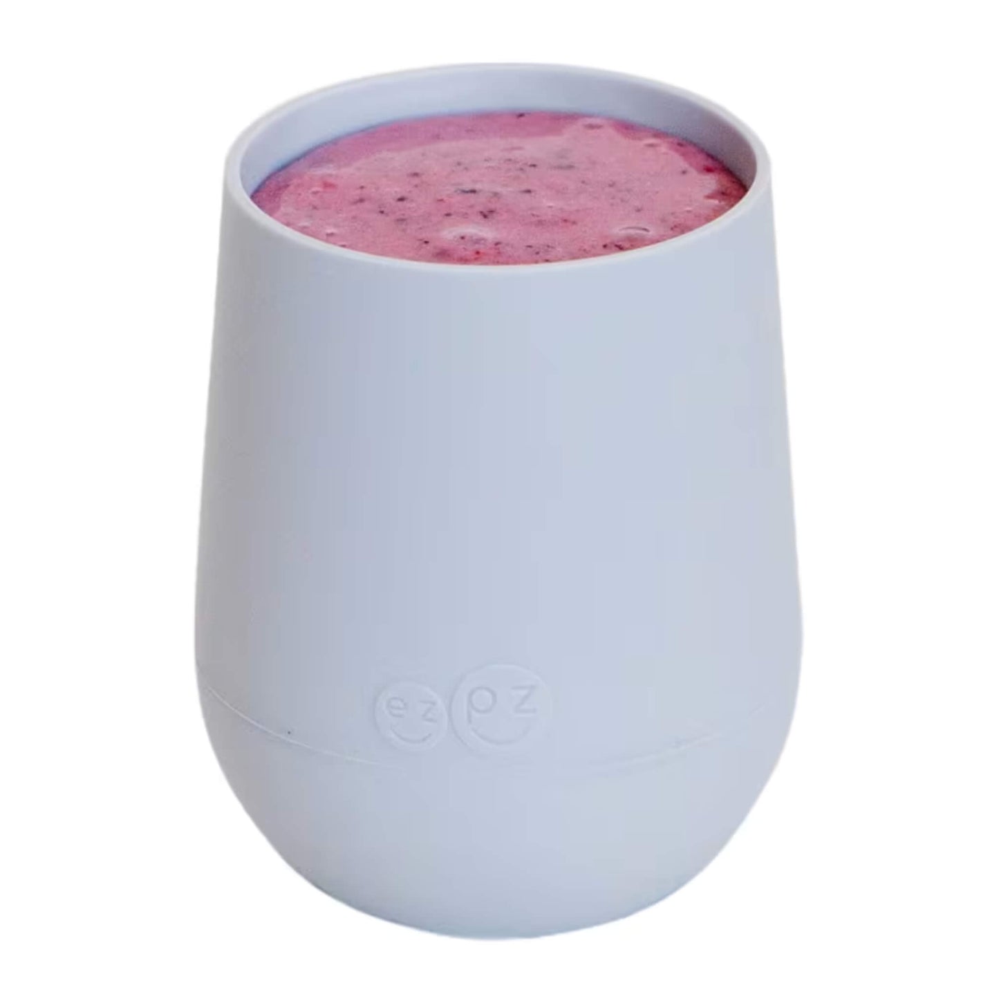 A pewter silicone training cup shown filled with milk, designed for toddlers learning to drink from an open cup.