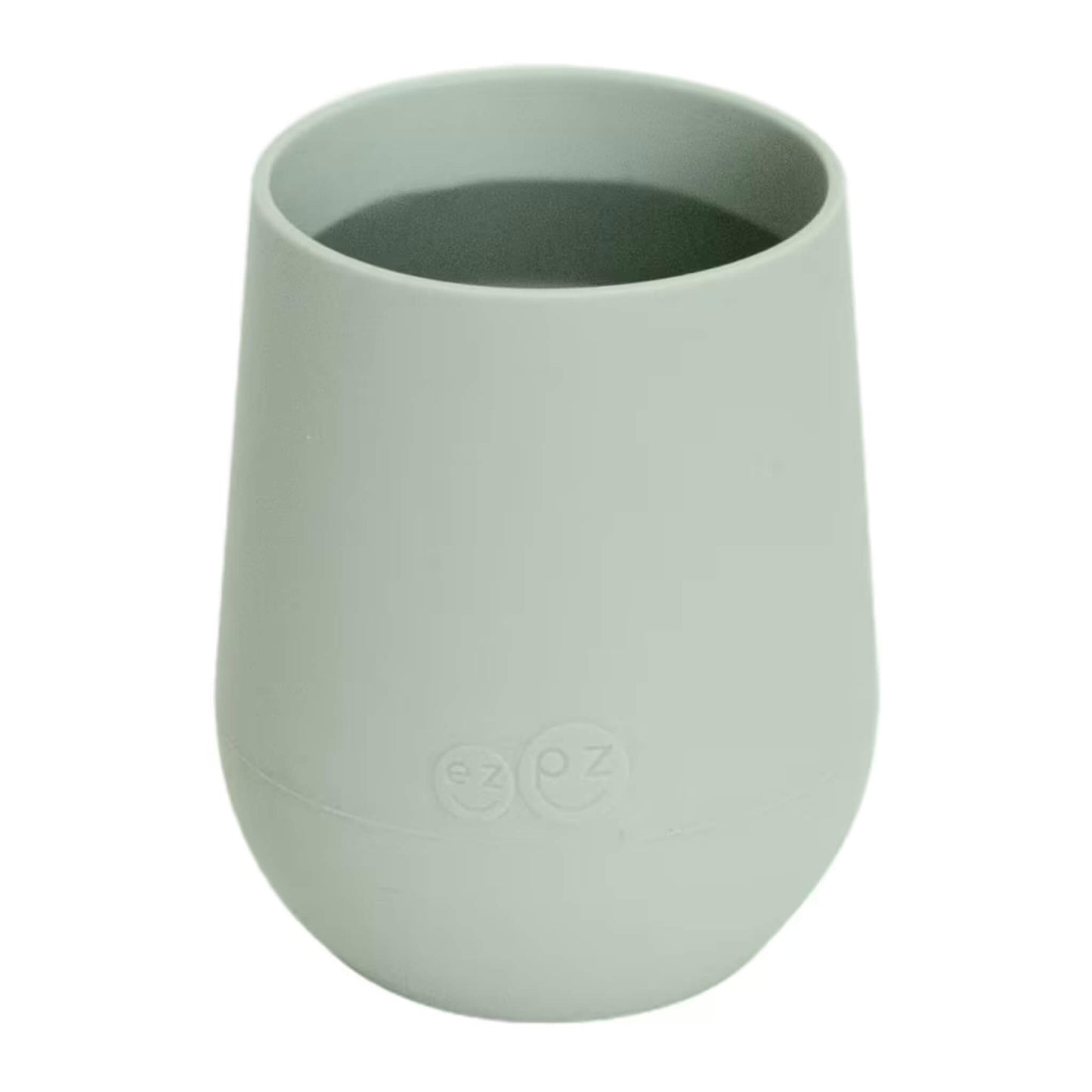 A sage green silicone training cup shown filled with milk, designed for toddlers learning to drink from an open cup.
