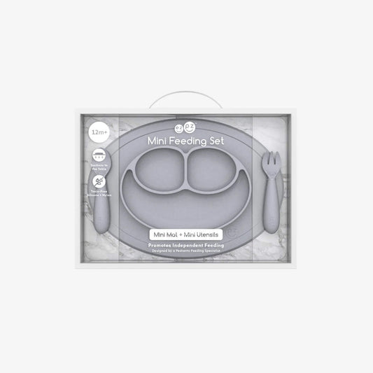 Boxed Ezpz Mini Feeding Set in Pewter displayed in retail packaging with the mat and utensils visible through the clear front.