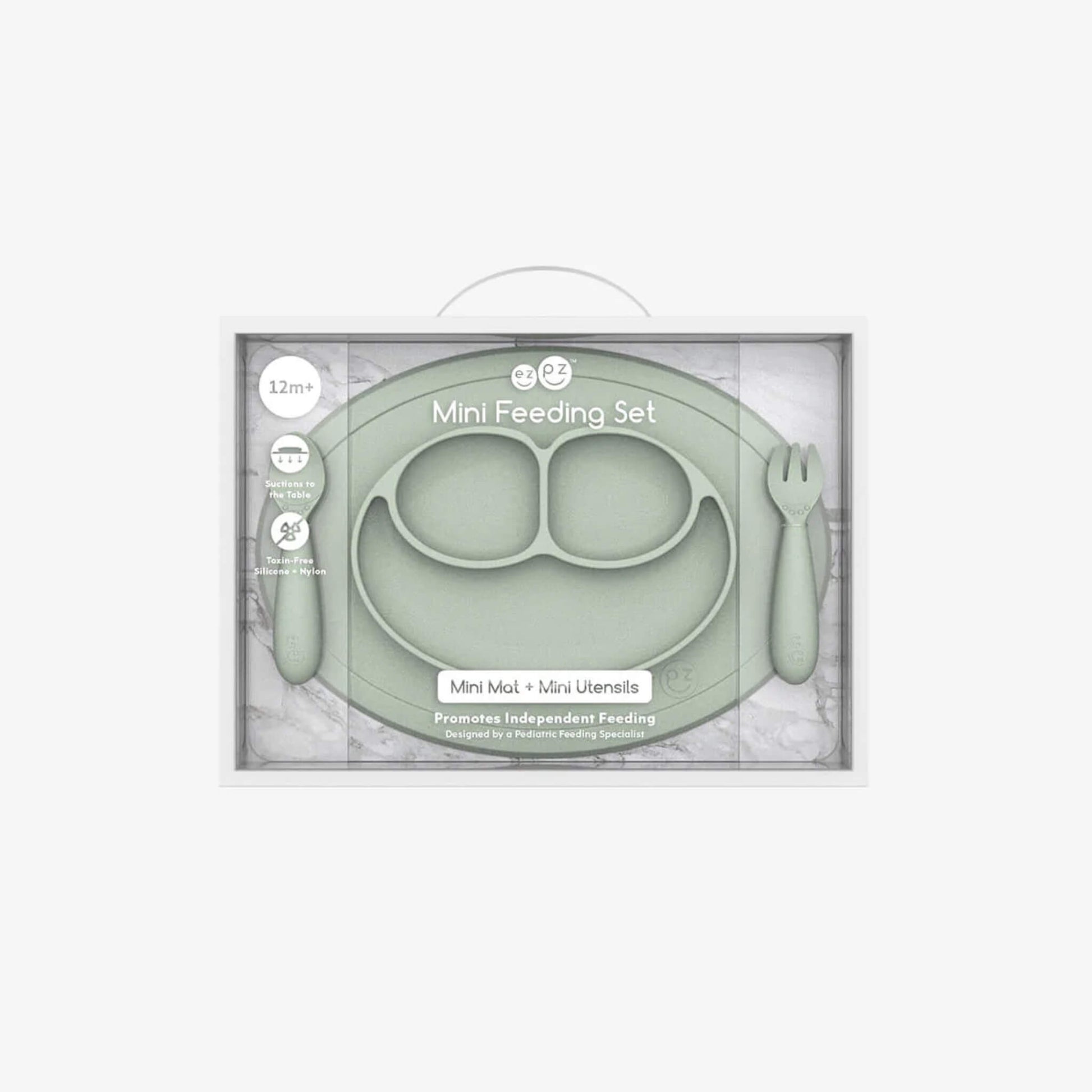 Boxed Ezpz Mini Feeding Set in Sage displayed in retail packaging with the mat and utensils visible through the clear front.